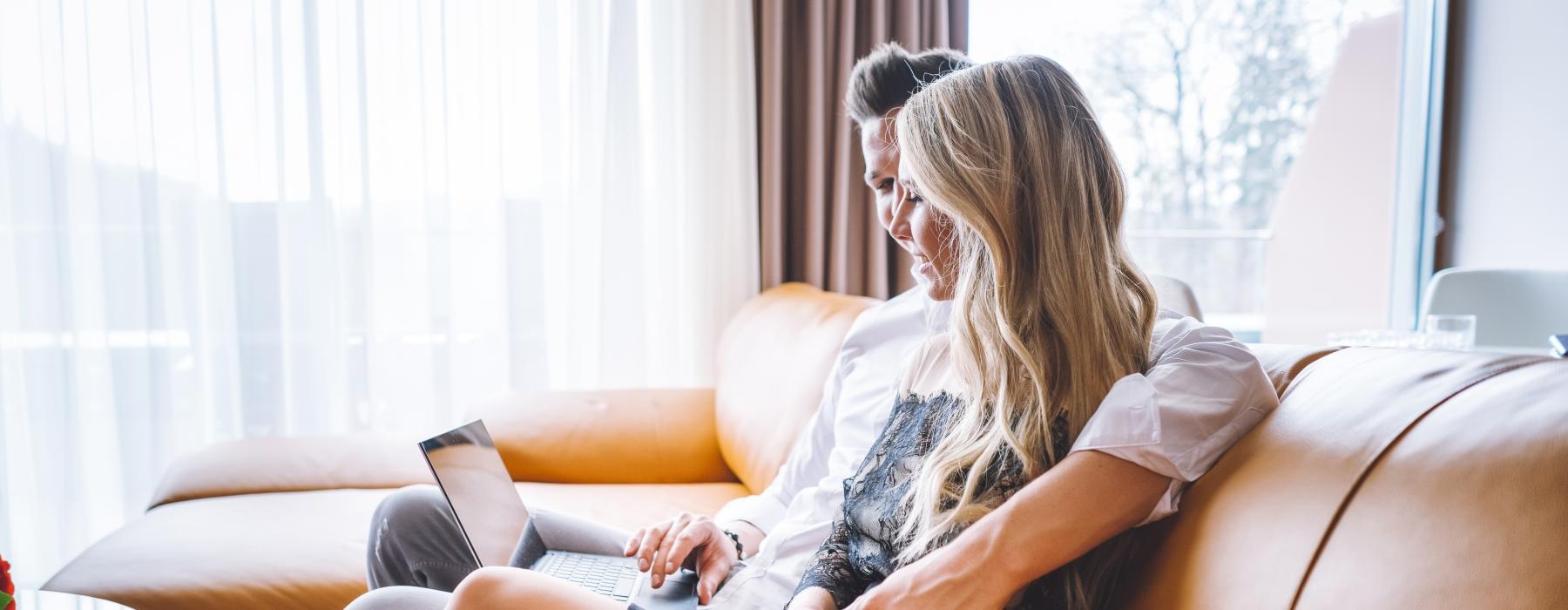 a couple sits on a couch and looks at laptop