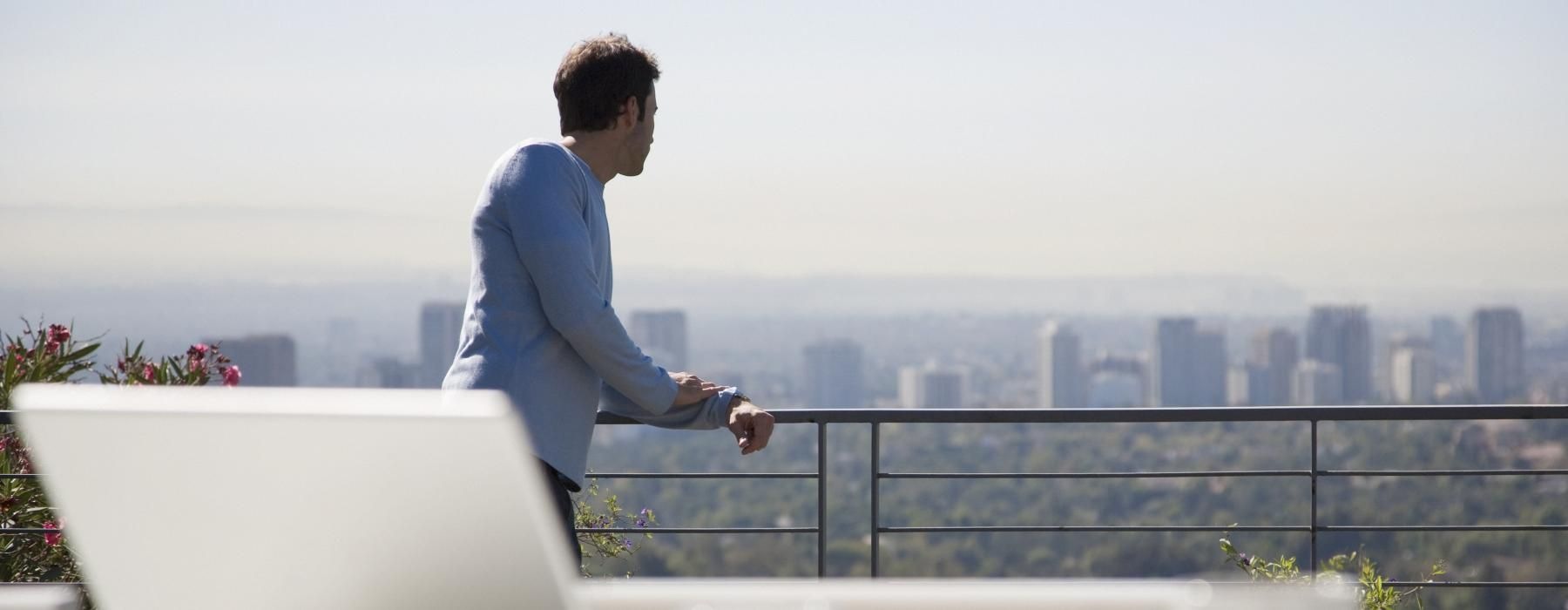 a man standing on a balcony near a table with a laptop