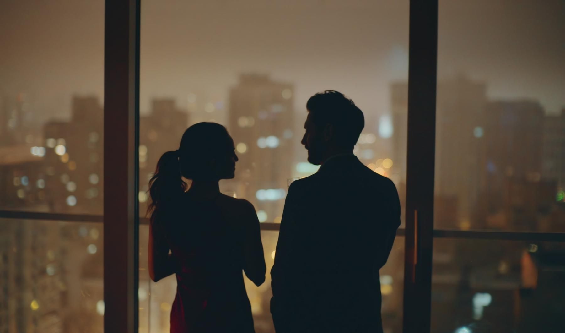 a man and woman standing next to each other and look out a window