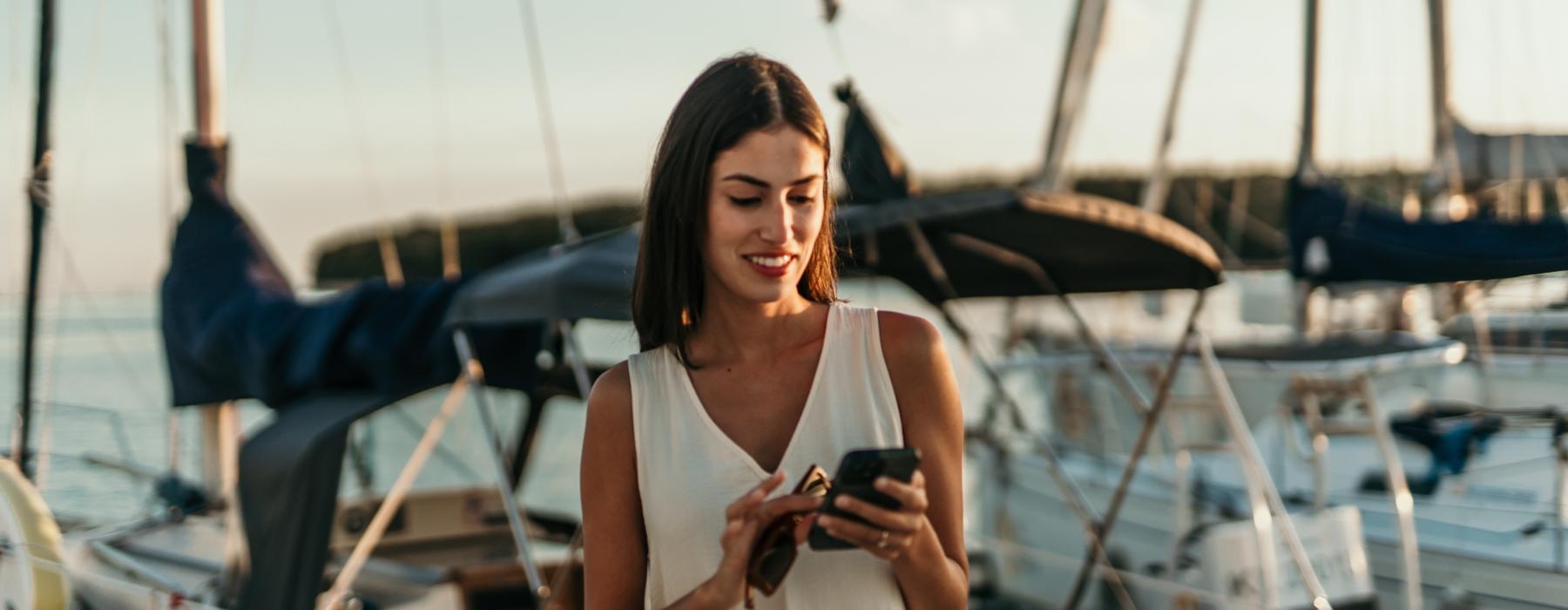 woman texting on a pier next to a boat